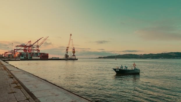 A fishing boat near a port with cranes at sunset, offering a serene view.