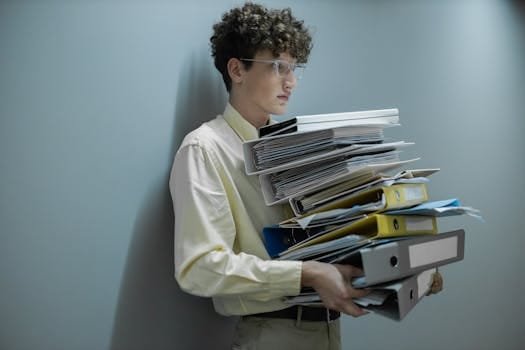 Capitan Vas Angajari 2026: Top Sfaturi pentru un Job Offshore de Vis + Ofertă Exclusivă Muncitori Platforme Petroliere! 4 An overworked office worker carrying a large stack of files and folders in a modern setting.