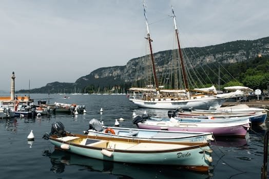 De la Zero la Navigator Profesionist: Cum un Curs pentru Maritimi i-a Schimbat Cariera în 2026 (Studiu de Caz) 2 A tranquil scene at Lake Garda harbor with boats and scenic cliffs.