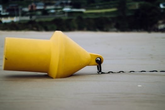 Ghidul Complet pentru Marinari: Cum să Găsești Rapid Locuri de Muncă pe Mare în 2026 3 Close-up of a yellow buoy with chain on a sandy beach, featuring a blurred background.