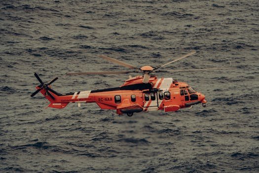 Ghidul Complet pentru Marinari: Cum să Găsești Rapid Locuri de Muncă pe Mare în 2026 4 Orange rescue helicopter in flight over ocean waves, conducting emergency operation.
