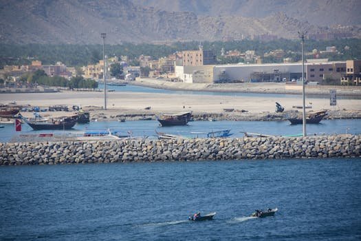 Offshore & Punte: Top Companii de Recrutare Marinari Comercianți în 2026 - Angajări Garantate! 3 A vibrant harbor scene at al-Chasab Musandam with boats and mountains in the background.