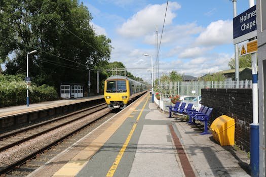 Train approaches Holmes Chapel station under a bright sky in Cheshire, UK.