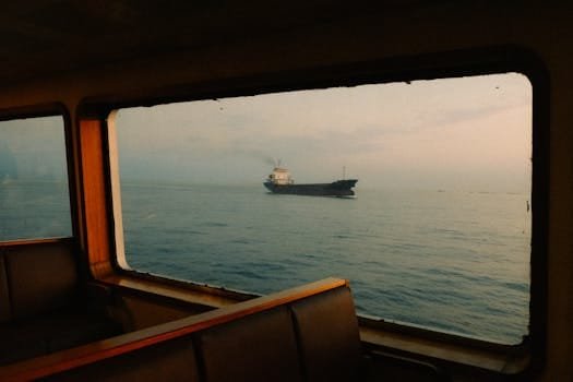 A serene view of a container ship on the sea through a cabin window, showcasing maritime travel.