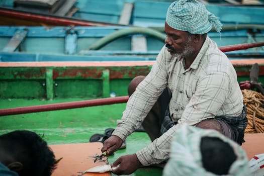 An elderly fisherman cleans fish on a colorful boat, showcasing traditional practices.