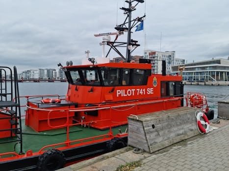 Vibrant red pilot boat docked in a harbor with urban backdrop.