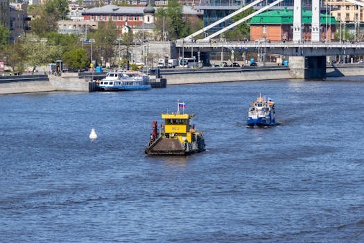 Riverboats navigate under a bustling city bridge, showcasing urban waterfront life.