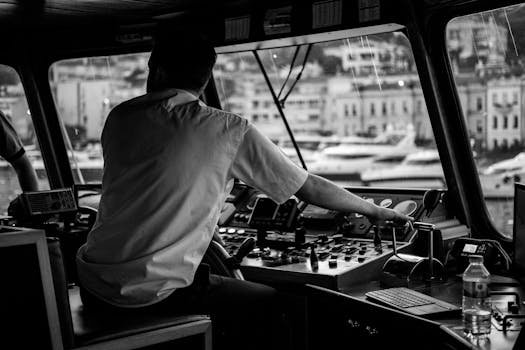 Cum să navighezi cu succes în cariera de ofițer de punte: ghid complet 6 An atmospheric black and white image of a captain navigating a vessel in a busy harbor environment.
