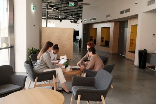 A modern office scene with four women discussing work around a table.