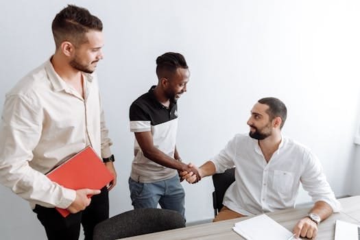 Three men in an office setting, shaking hands, representing teamwork and diversity.