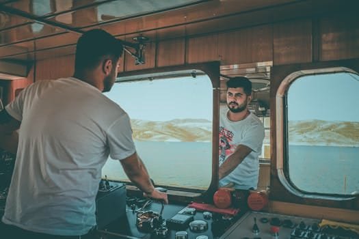 Ce este Certificatul STCW Manila pentru Ofițeri de Mașină și Cum Influențează Cariera Maritimă 2 Man piloting boat indoors, reflected in mirror, with ocean backdrop.