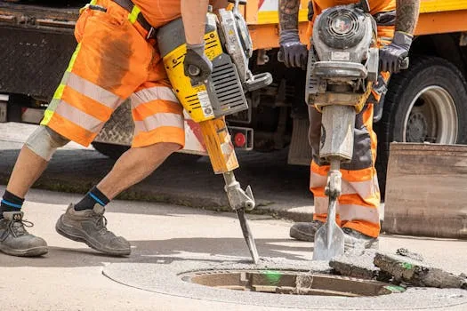 Cum să Alegi Lungimea Optimă a Contractului de Navigație Maritimă pentru Marinari 3 Construction workers repairing road with heavy tools, emphasizing urban development.