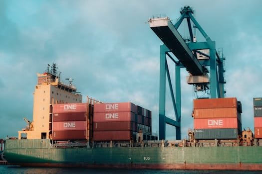Cum să Compari Contractele de Navigație Ofițeri Mașină: Remunerare și Condiții 2 Large cargo ship loaded with colorful containers at a bustling industrial port.