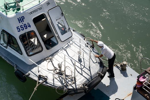 Aerial view of a man securing a boat with ropes in a busy harbor. Daytime setting with clear water.