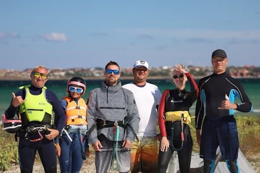 Cum să Evaluezi Oferta de Locuri de Muncă Marine Cargo Transport în România 4 A diverse group of surfers in wetsuits and life vests posing happily by the ocean shore on a sunny day.