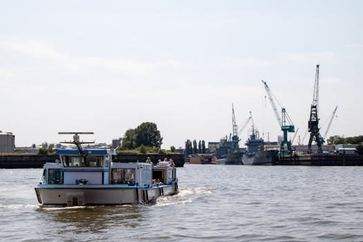 A lively harbor scene in Hamburg with a boat sailing and construction cranes in the background.
