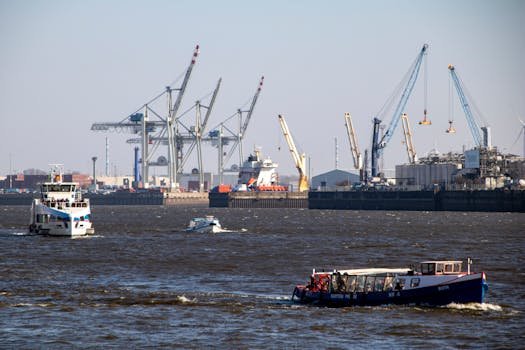 Dynamic scene of boats and cranes in Hamburg's bustling Elbe port under a blue sky.