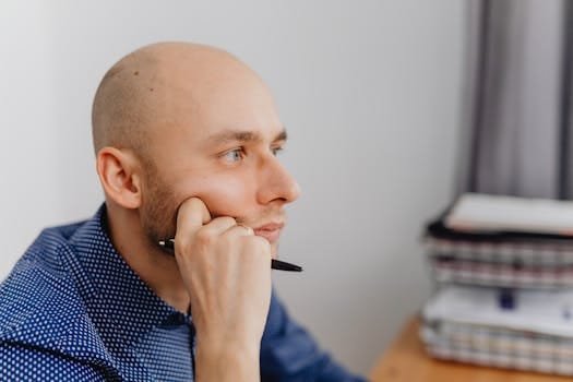 Cum să Obții un Certificat de Competență pentru Ofițerii de Punte și Mașină în România 2 Bald man in an office thinking deeply with a pen in hand near a desk.