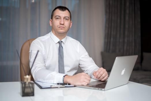 Cum să Obții un Certificat de Competență pentru Ofițerii de Punte și Mașină în România 3 A confident businessman in corporate attire working diligently on a laptop in a modern office setting.