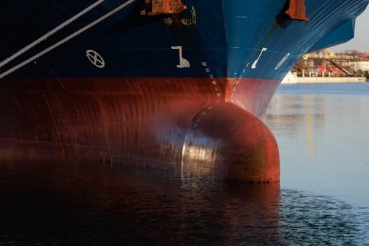 Cum să Optimizezi Salariul Mecanicului Naval în Funcție de Experiență în România 3 Close-up of cargo ship bow in industrial harbor reflecting on calm water.