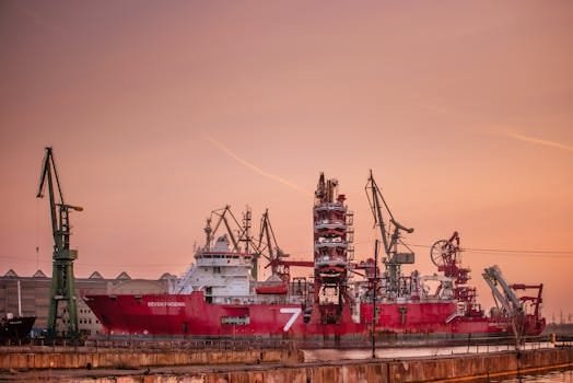 Cum să Optimizezi Salariul Mecanicului Naval în Funcție de Experiență în România 4 Industrial ship moored in Gdańsk harbor at sunset with cranes in view.