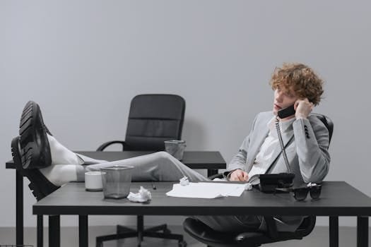 Businessman in gray suit casually talking on phone with feet on desk, showcasing laid-back office setting.