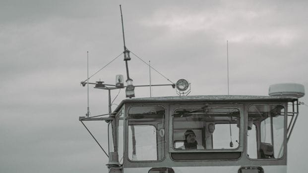 Ce este Cursul SSM Ofițer Maritim Certificat pentru Începători în România 4 A captain stands on the bridge of a ship, navigating through cloudy weather.