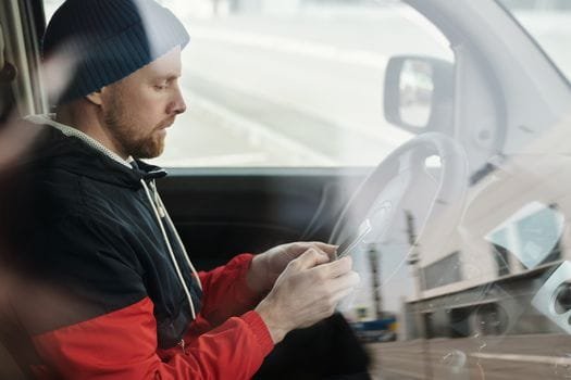 Man sitting in a car using a smartphone, reflecting urban lifestyle. Side view.