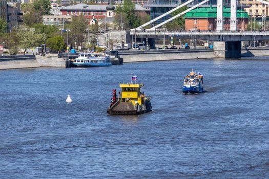 Cum să Compari Agențiile Crewing Marinari pentru a Alege Contractul de Navigație Potrivit 3 Riverboats navigate under a bustling city bridge, showcasing urban waterfront life.