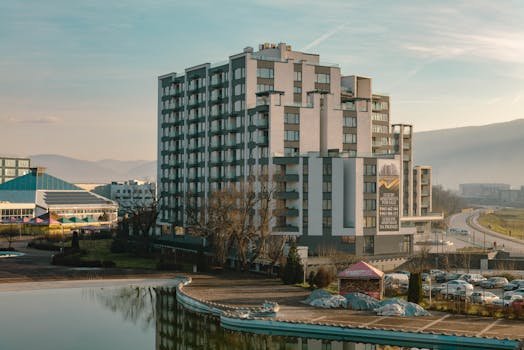 Cum să Optimizăm Diferența dintre Salariul Brut și Net în Contractele Ofițerilor Maritimi 2 Explore a modern residential building with a serene pond and scenic mountain backdrop, ideal for urban living.
