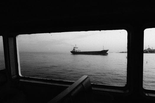 Ghid Complet: Cele Mai Bune Servicii de Recrutare Ofițeri Punte prin Agenții Crewing 2 A monochrome view through a window of a container ship sailing on calm sea waters.