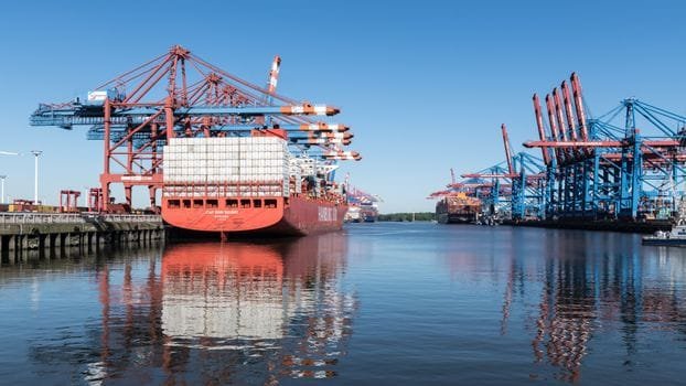Pași pentru Alegerea între Pozițiile de Ofițer Punte și Mașină: Salarii și Certificări 2 Vibrant container ship docked at Hamburg harbor, reflecting on calm water under a clear blue sky.