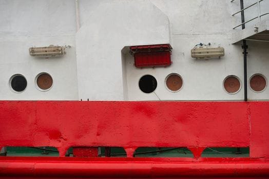 Pași pentru Negocierea Condițiilor în Contractul Maritim Ofițer Punte România 2 Detailed view of a ship's red hull and white body featuring round portholes and safety equipment.