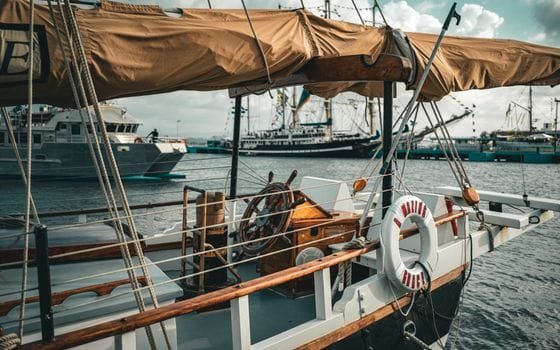 Top 5 Cursuri Certificare GMDSS Maritim pentru Frecvențe Radio: Alegerea Ideală 4 A rustic sailboat docked in a bustling maritime harbor, showcasing nautical charm.