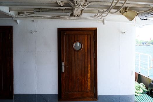 Close-up of a wooden door with porthole on a vessel deck, offering a nautical theme.