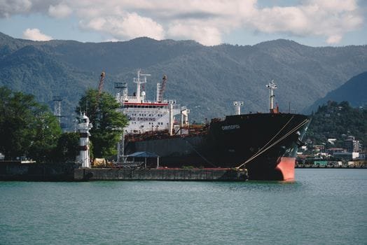 A large cargo ship docks at a picturesque port with mountains in the background, highlighting maritime transport.