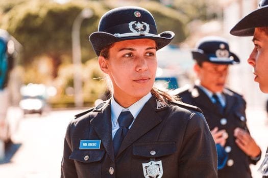 A young policewoman in uniform stands attentively outdoors during the day.