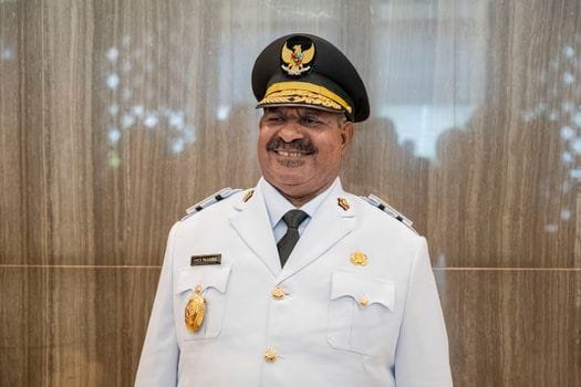 Indonesian military officer smiling in formal white uniform indoors, Papua, Indonesia.