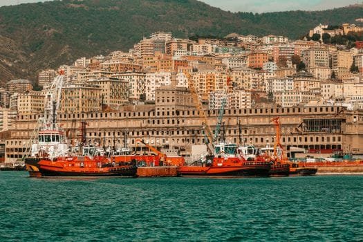 Explore the bustling waterfront of Genoa, Italy, with bright boats and historic architecture against a hillside backdrop.