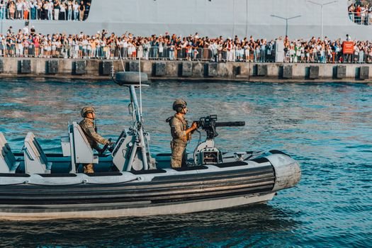 Cum influențează agențiile de crewing din Constanța obținerea de 'navigator jobs' pe termen lung? 4 A military boat with armed soldiers patrolling near a crowded pier during a public event.