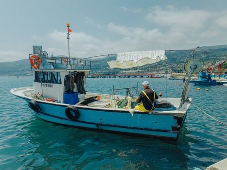 Top 5 Oportunități de Joburi în Catering la Bordul Navelor pentru August 2026 3 A tranquil scene of a fisherman sitting on a moored fishing boat in Sinop, Türkiye under a clear blue sky.