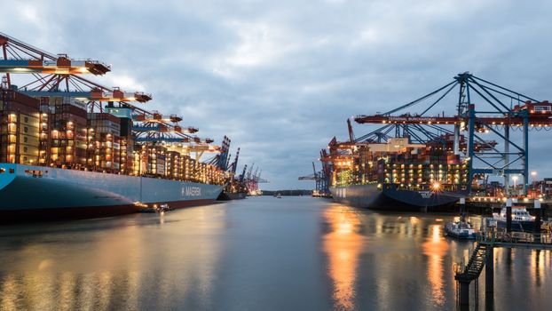 Top 5 Poziții Entry Level în Navigație pentru Tinerii Marinari din România, August 2026 4 Container ships and cranes at Hamburg harbor at dusk, showcasing industrial freight transport.