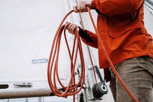 Close-up of a sailor handling ropes on a sailing boat, showcasing nautical skills and equipment.