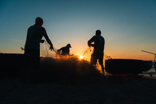 Ce certificări trebuie să ai pentru a accesa joburi prin 'jobs and sea' în România? 4 Silhouetted fishermen sorting nets against a vibrant sunset on a Vietnamese beach.