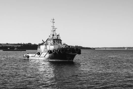 A black and white photo of a tugboat navigating the calm sea near the coast.